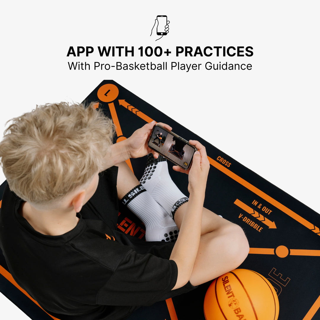 A client sitting comfortably on a training mat, focused on a smartphone or tablet displaying a SilentBall Academy video training session from the app