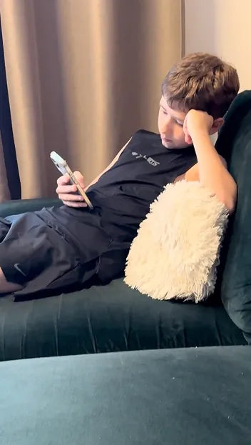 Person lying on a couch using a smartphone with a beige pillow beside them.